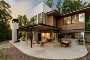 A luxury home in the woods with a patio going around it.