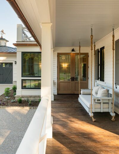 Custom wrap-around porch with porch swing, energy-efficient luxury home near Asheville, NC, featuring locally milled wood, exposed beams, and natural elements from original farmhouse.