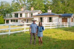 Homeowners in front of remodeled, energy-efficient house with luxury home builder near Asheville, North Carolina, featuring original farmhouse aspects, locally milled wood, exposed beams, and natural elements.