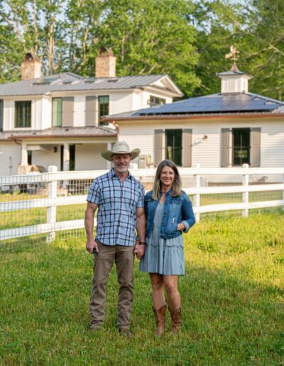 Homeowners in front of remodeled, energy-efficient house with luxury home builder near Asheville, North Carolina, featuring original farmhouse aspects, locally milled wood, exposed beams, and natural elements.